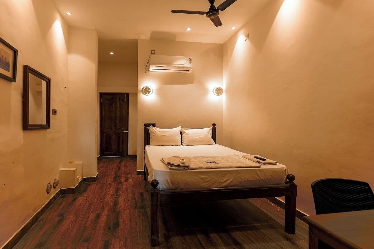 A bedroom with a bed, a ceiling fan, an air conditioning unit, and a wooden floor.