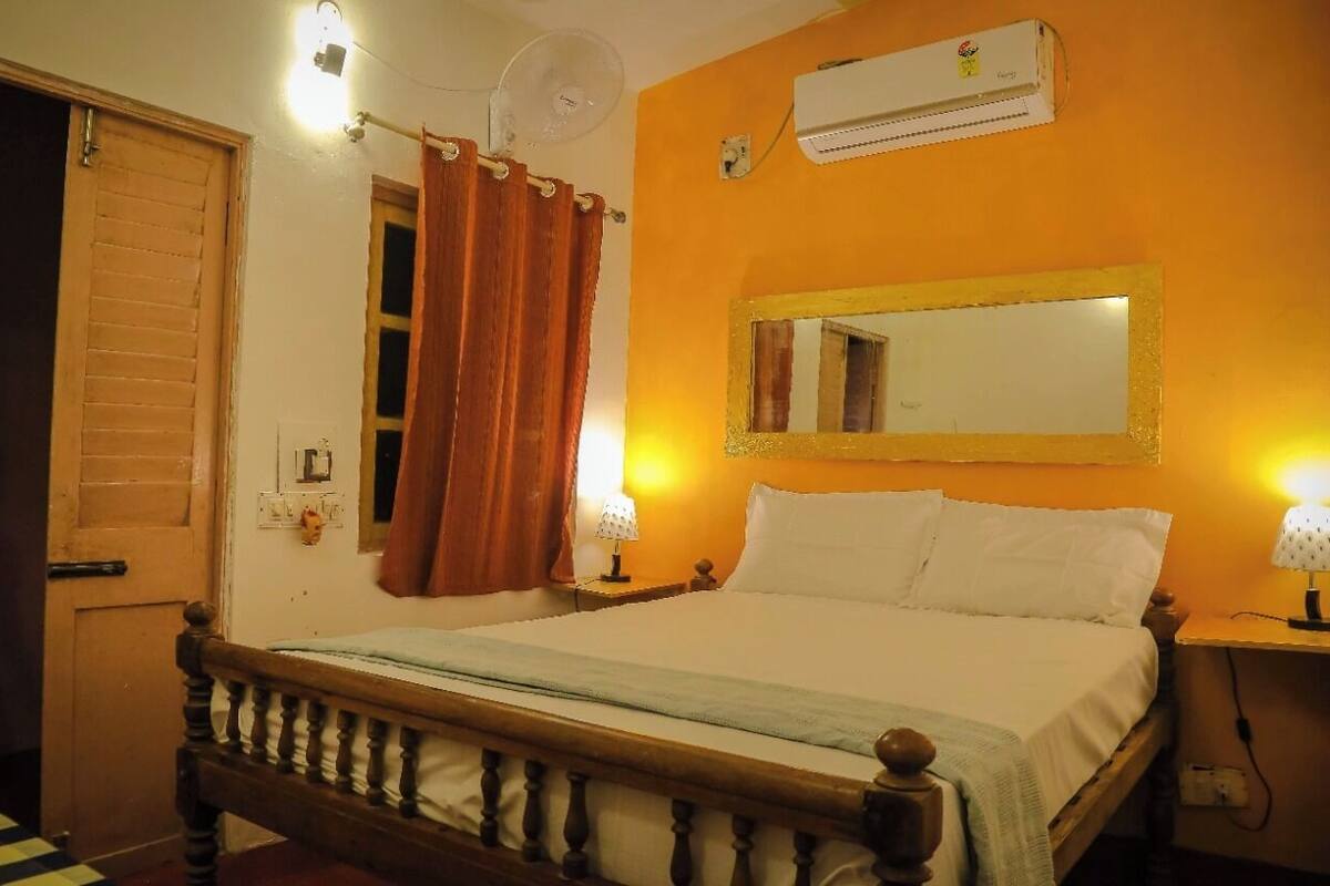 A bedroom with a wooden bed, a ceiling fan, an air conditioner, and a mirror on the wall.