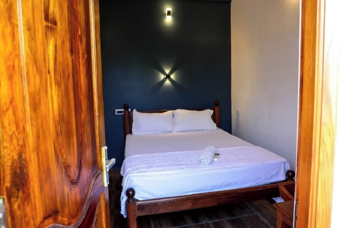 A neatly made bed with white linens and a rolled towel, a wooden headboard, and a small bedside table.