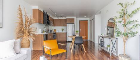 Una sala de estar moderna con un sofá, una mesa de comedor con sillas, una zona de cocina con armarios y electrodomésticos, y una planta en maceta.