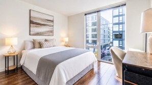 A modern hotel room with a large bed, two bedside tables with lamps, a view of the city through a large window, and a cityscape visible through the window. - Seattle`s modern and stylish Penthouse Apartment- Wifi, Pet Friendly, Rooftop (Seattle)