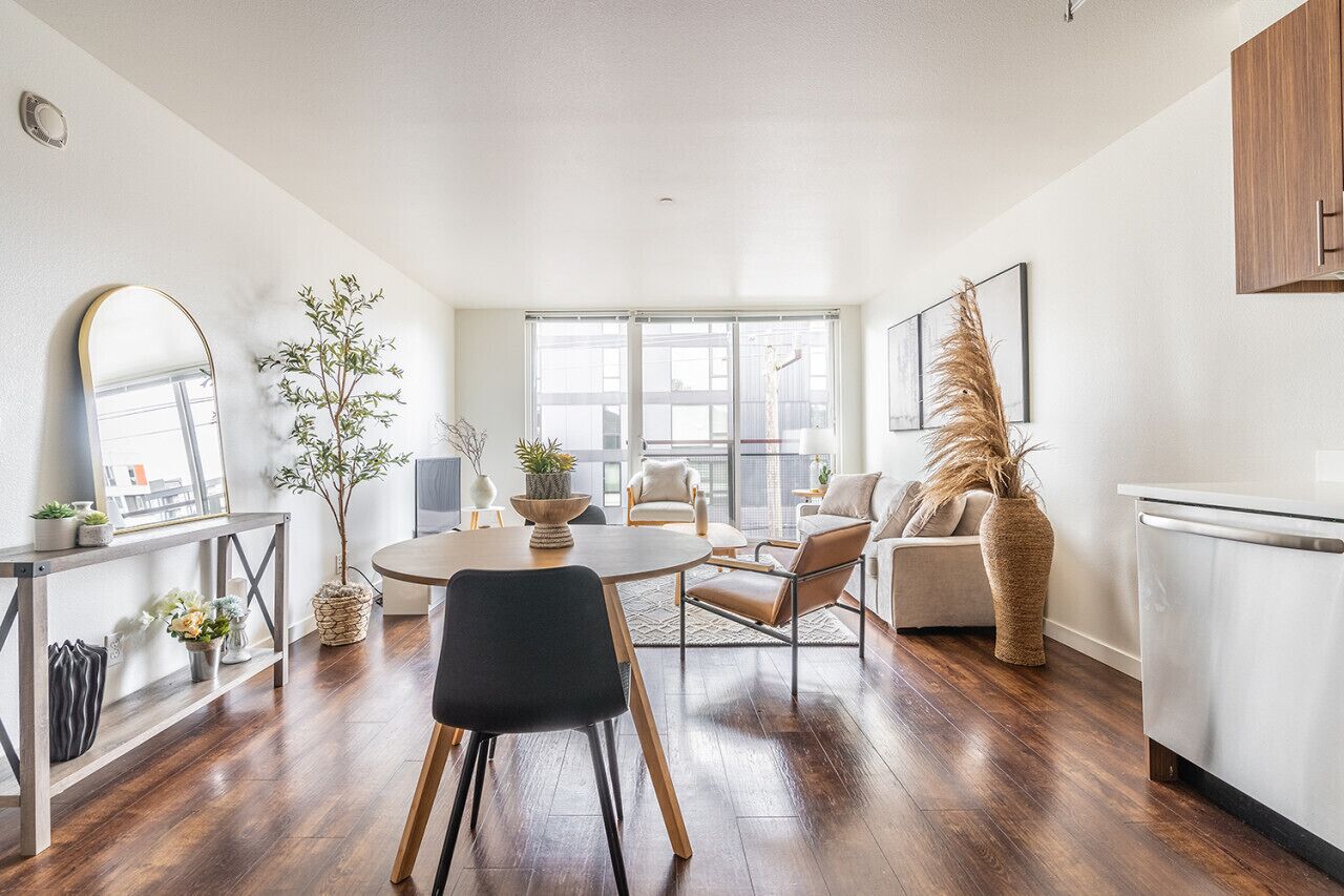 A modern living room with a dining table, chairs, a sofa, and a kitchen area.