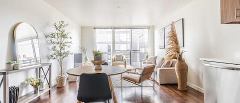 A modern living room with a dining table, chairs, a sofa, and a kitchen area.