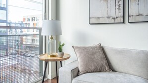 A modern living room with a grey sofa, a round wooden side table with a lamp, and two framed nature paintings on the wall. - Seattle`s modern and stylish Penthouse Apartment- Wifi, Pet Friendly, Rooftop (Seattle)
