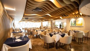 A modern hotel dining area with tables set for guests, a unique ceiling design, and a view of the hotel lobby. - Pearl Hotel Dhaka (Dhaka)