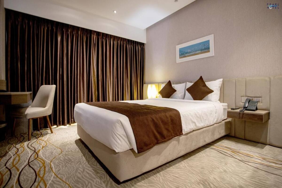 A hotel room with a large bed, a chair, a bedside table with a phone, and a curtain backdrop.