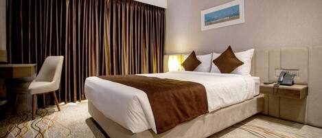 A hotel room with a large bed, a chair, a bedside table with a phone, and a curtain backdrop.