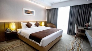 A hotel room with a large bed, a desk, a chair, a lamp, and a painting on the wall. - Pearl Hotel Dhaka (Dhaka)