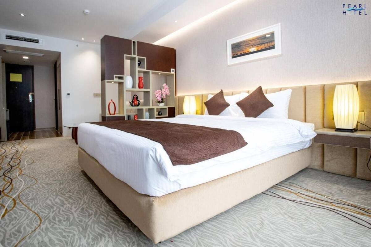 A hotel room with a large bed, bedside tables, a built-in shelf unit, and a framed picture on the wall.