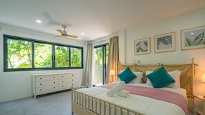 Ein Schlafzimmer mit Bett, Nachttisch, Kommode und großen Fenstern mit Vorhängen.