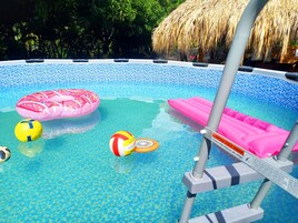 Una piscina con juguetes inflables y una estructura de techo de paja.