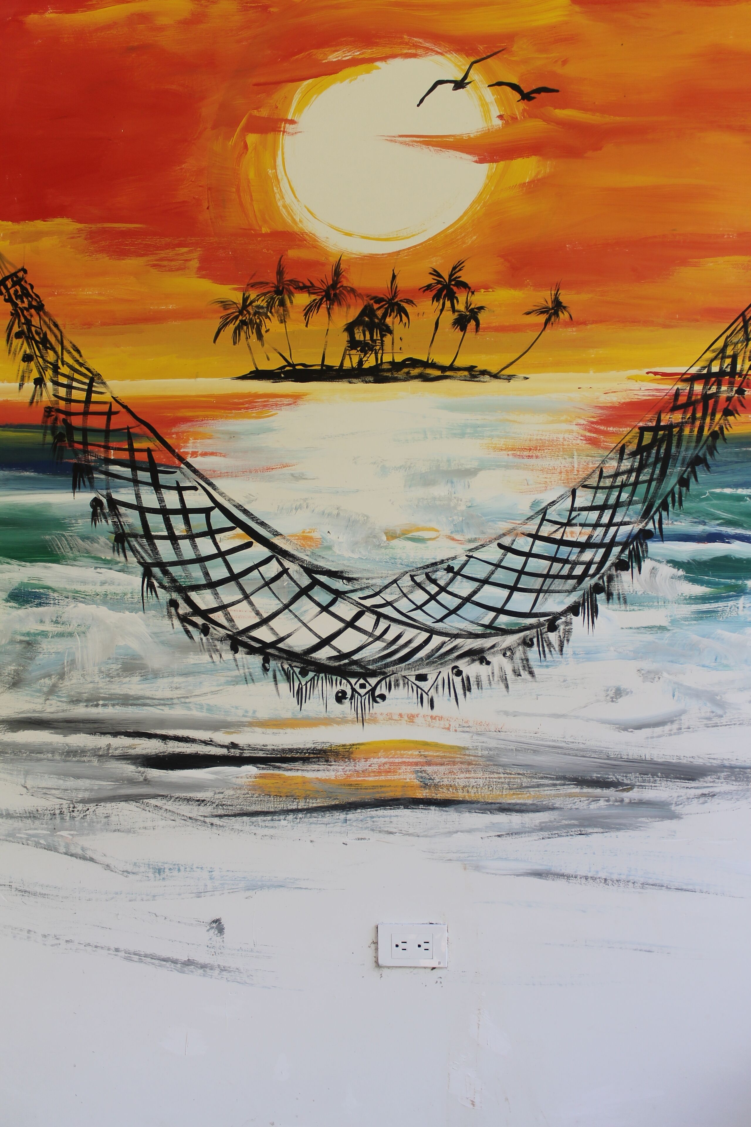 A hammock on a beach with a sunset and palm trees in the background.