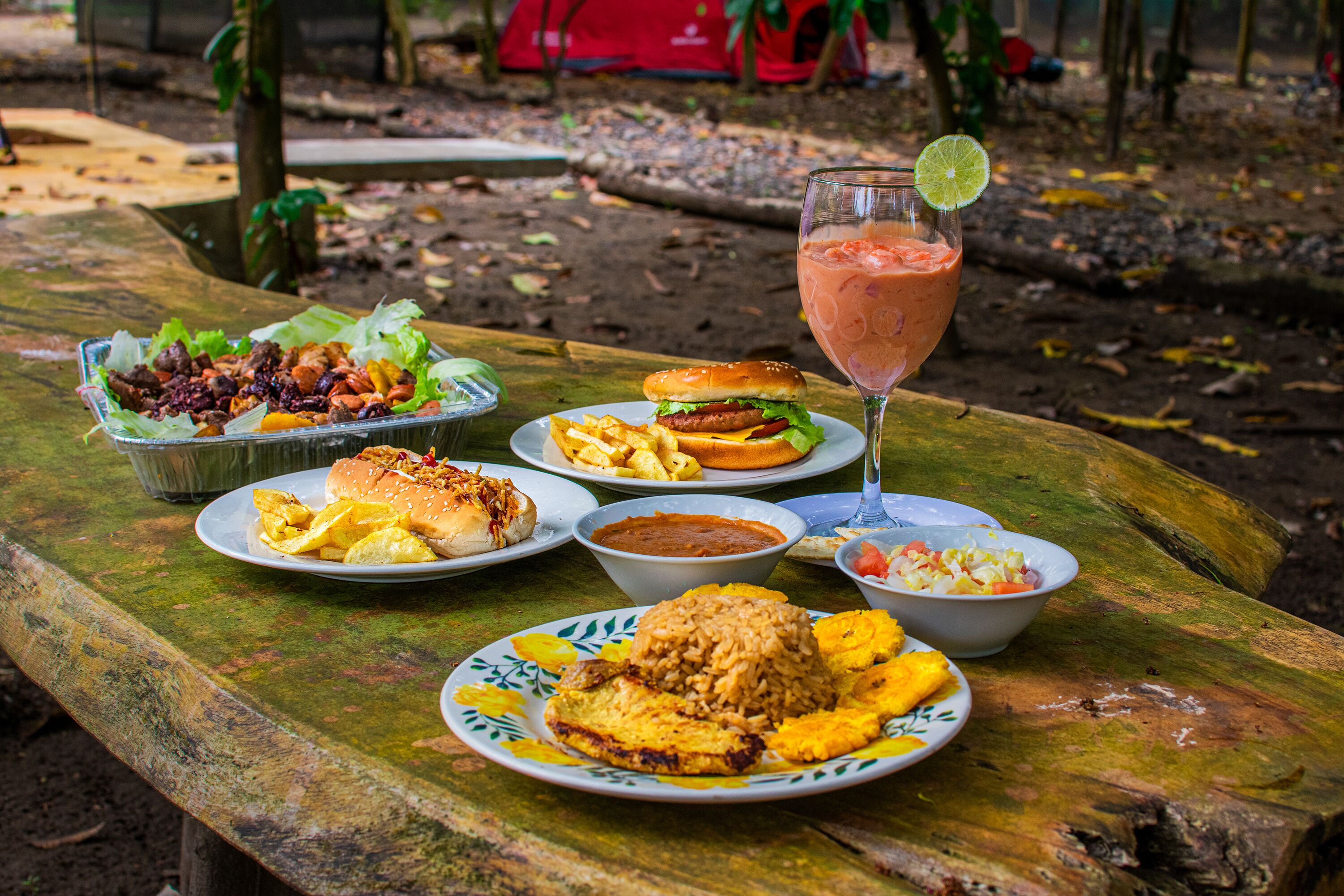 A picnic table with various dishes including a burger, salad, rice, and a drink.