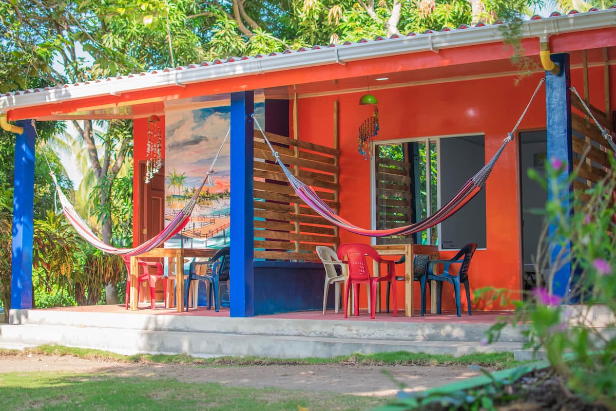 Un bâtiment aux couleurs vives, doté d’un porche abrité, d’un hamac et de chaises en plastique.