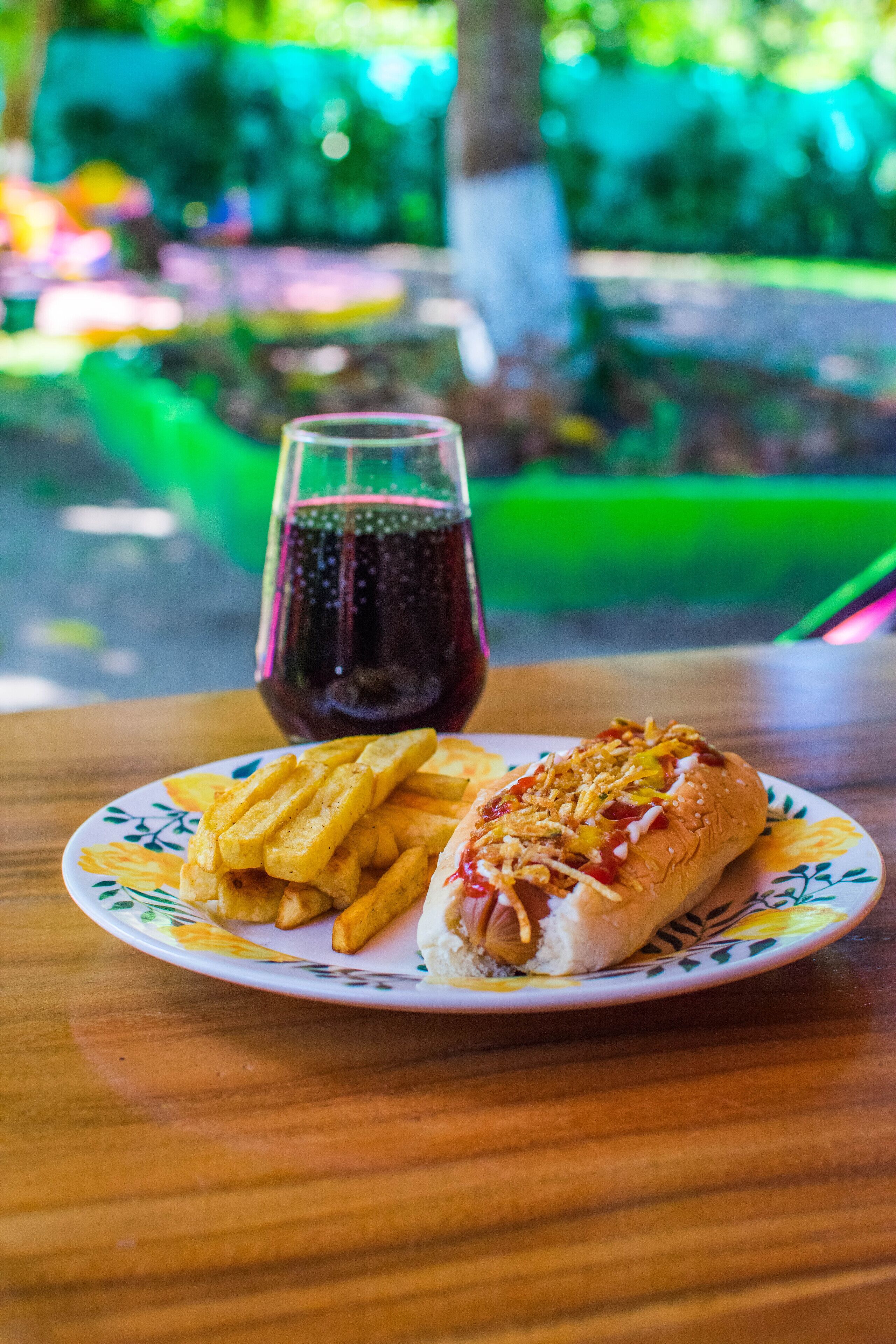 A plate with a hot dog and fries on a table with a glass of soda.