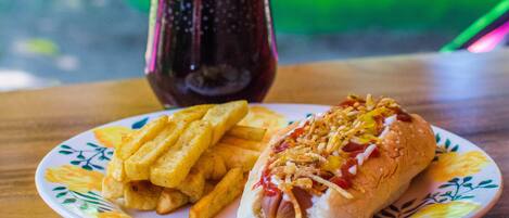 A plate with a hot dog and fries on a table with a glass of soda.