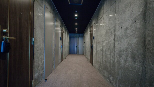 A hallway with concrete walls, wooden doors, and a carpeted floor. - ASCEND 101 (Asahikawa)