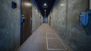 En hall med betongväggar, ett mattbeklätt golv och en dörr på vänster sida.