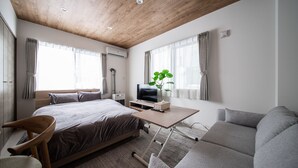 Ett modernt sovrum med ett träpanelat tak, en säng, ett skrivbord, en stol, en soffa och en krukväxt.