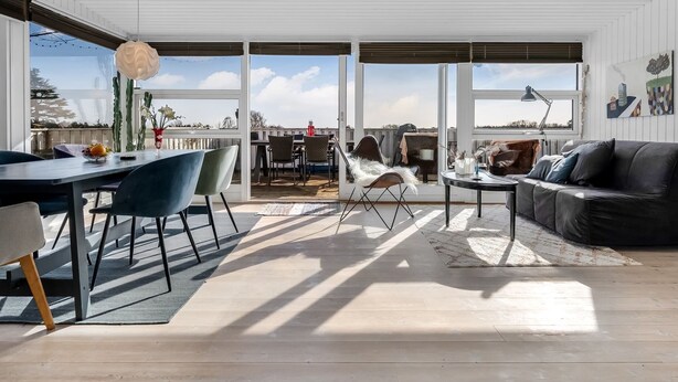 Amplia sala de estar con mesa de comedor, sillas, sofá y ventanas grandes que ofrecen vistas al exterior.