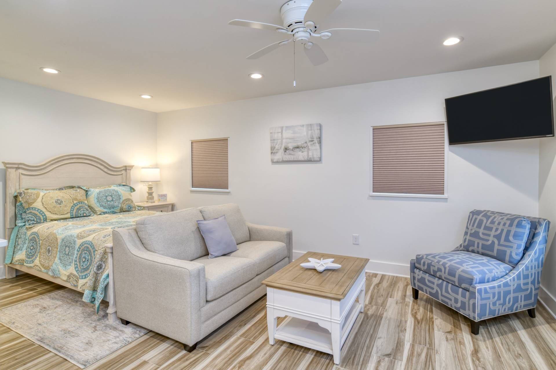 A bedroom with a bed, a sofa, a chair, a small table, and a ceiling fan.
