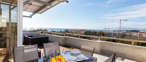 A balcony with a glass table, chairs, and a bowl of fruit.