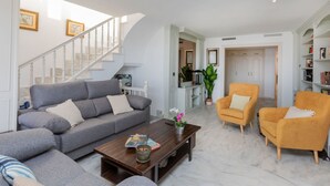 A living room with a grey sofa, a wooden coffee table, and two yellow armchairs. A staircase with white railings leads to a hallway. - Luxury Atic Cambrils by Interhome (Cambrils)