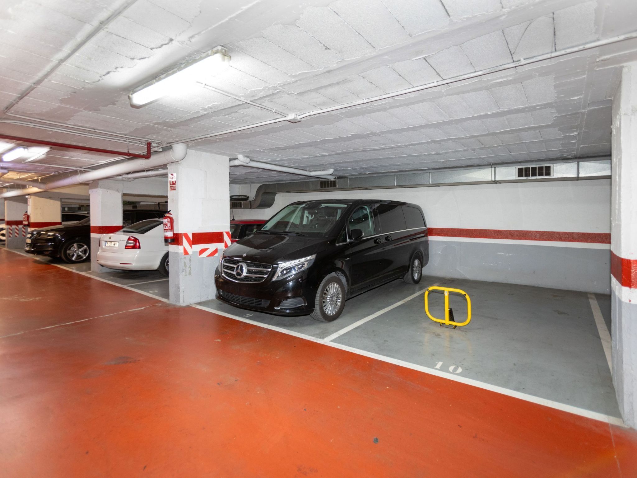 A parking garage with a black van parked in a bay, white walls, and red and white striped columns.