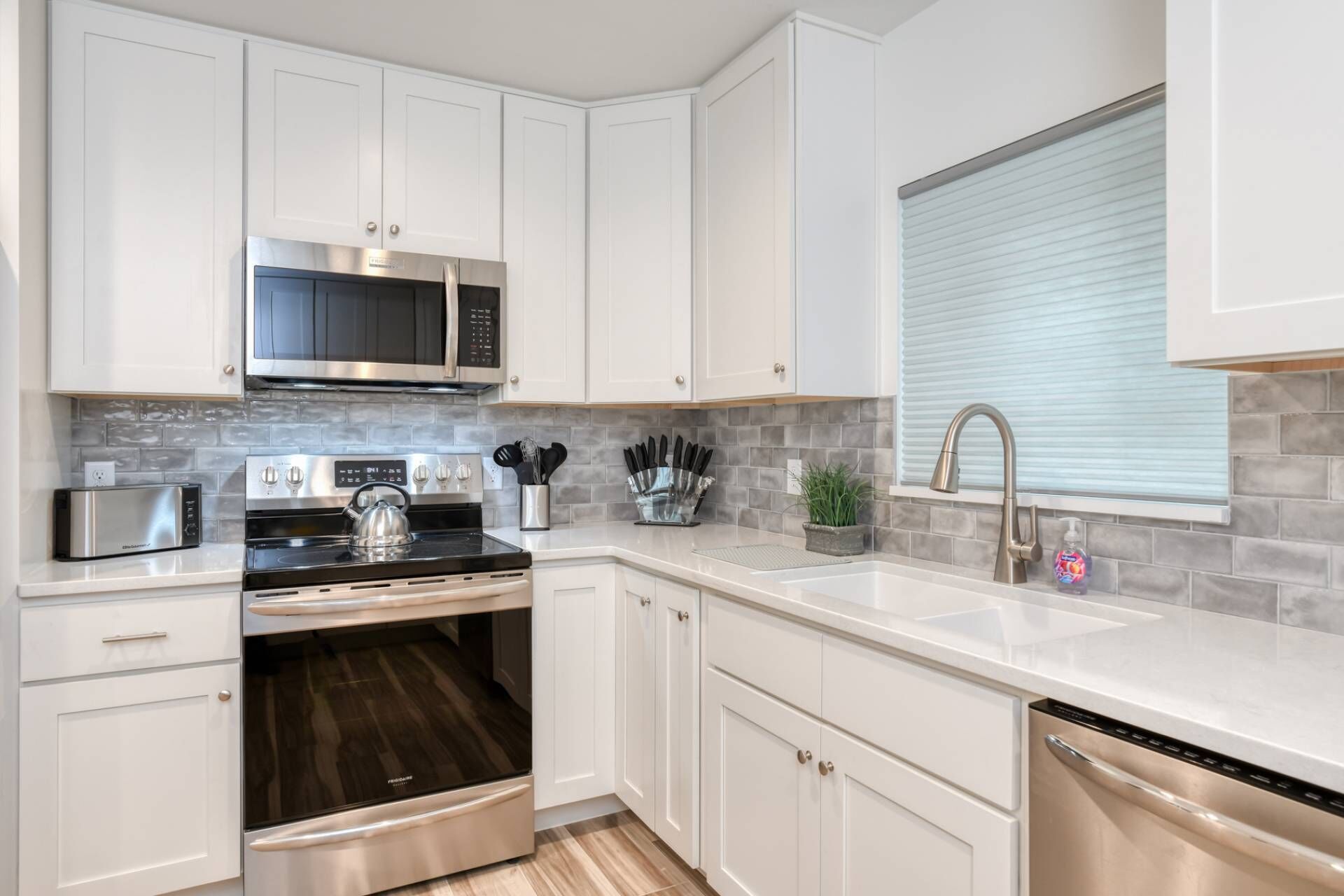 Una cocina moderna con armarios blancos, electrodomésticos de acero inoxidable y un salpicadero de azulejos grises.