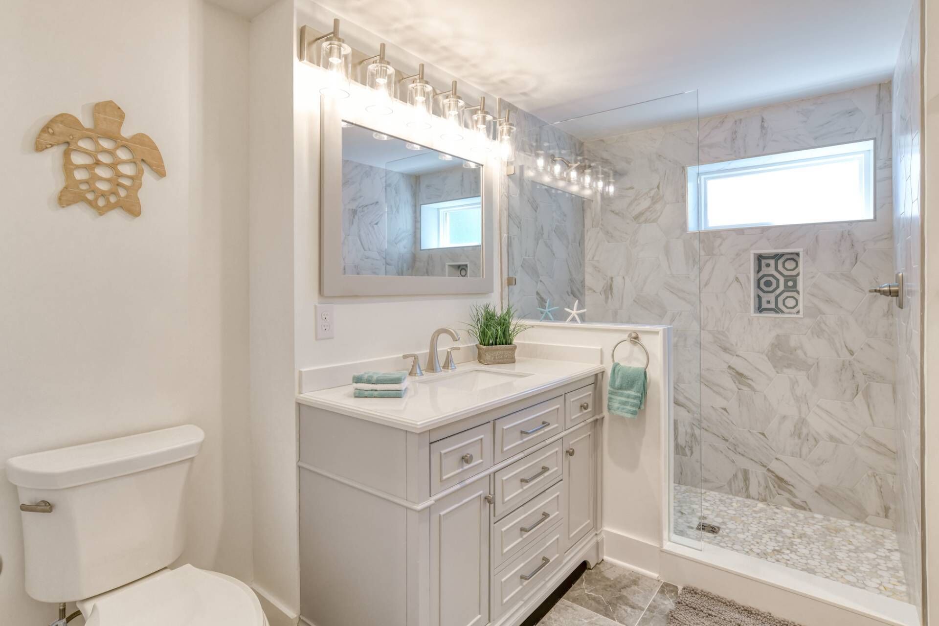 A bathroom with a marble wall, a vanity with a mirror, a sink, and a shower area.