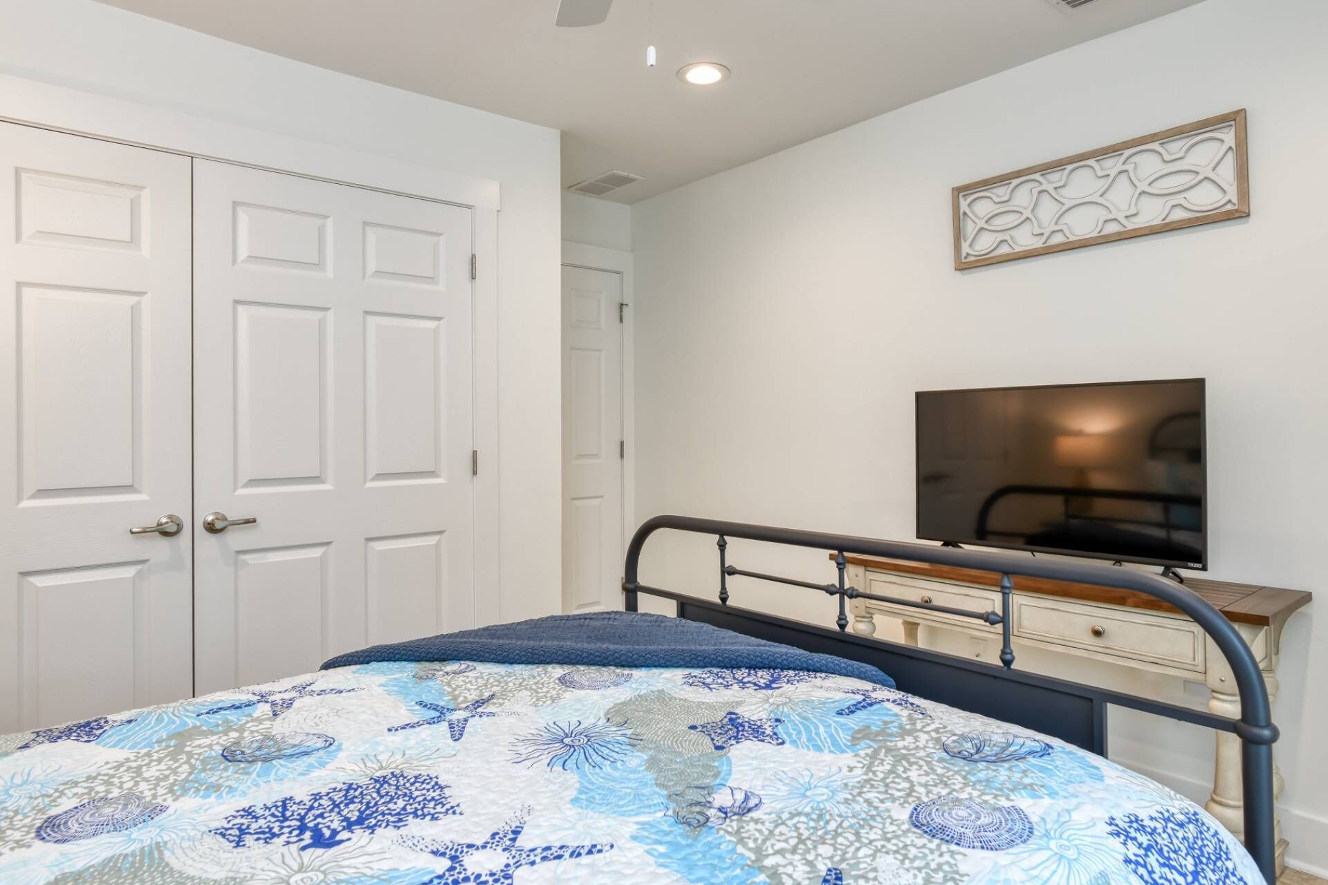 Un dormitorio con cama, televisión, cómoda y un juego de puertas blancas.