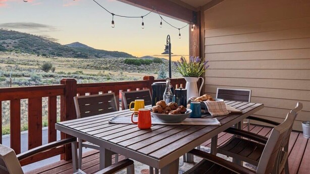 Eine Holzterrasse mit gedecktem Tisch für ein Frühstück, mit Blick auf eine Berglandschaft.