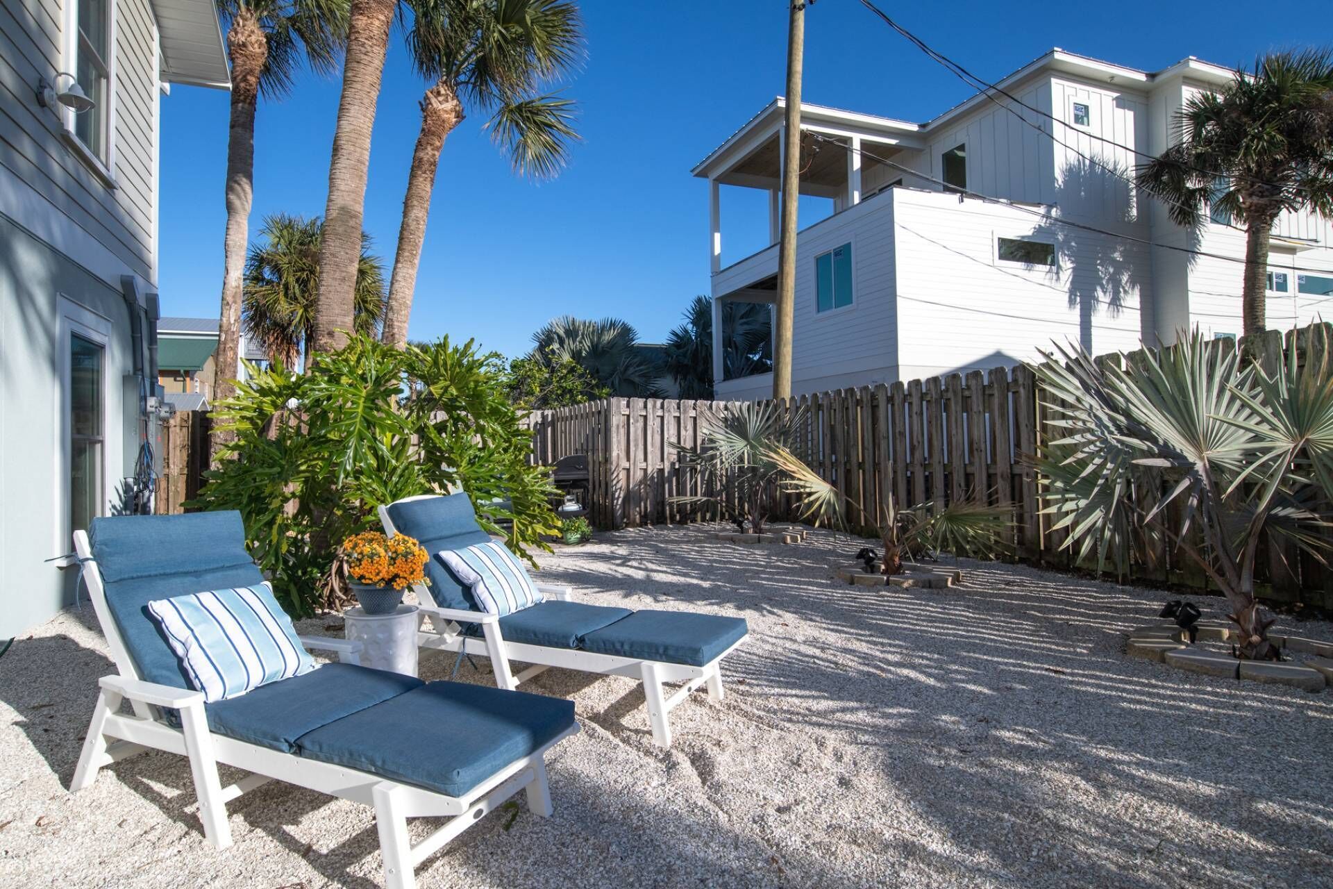 A backyard with two lounge chairs, a wooden fence, and tropical plants.