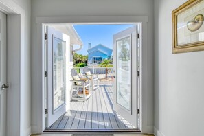 A view from inside a house to an outdoor deck with a table and chairs, a blue house in the background, and a framed picture on the wall. - Maritime Place Unit B (St. Augustine)