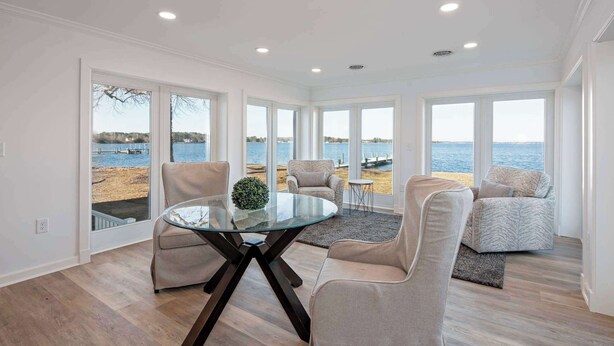 Una habitación amplia con una mesa y sillas de vidrio, ventanas grandes con vista a la playa y una decoración interior moderna.