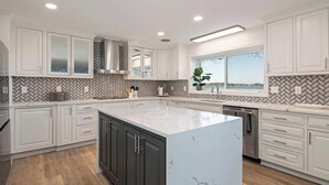Una cocina moderna con armarios blancos, una isla de mármol y un salpicadero con diseño en espiga.