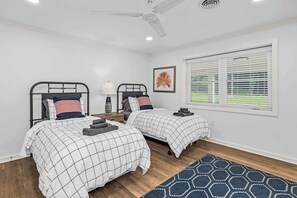 A bedroom with two beds, a ceiling fan, a window with blinds, and a rug.