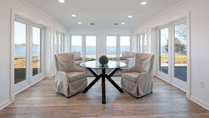 Una habitación espaciosa con una mesa redonda de vidrio, dos sillones color beige y grandes ventanales con vistas al mar.