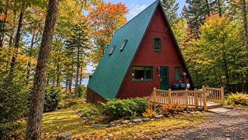 A red cabin with a green roof surrounded by trees and a wooden deck.