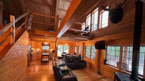 A log cabin interior with a fireplace, wooden floors, a dining area, and a kitchen. - Prong Pond Cabin*Water Access*Pet Friendly*Snowmobile Access (Greenville)