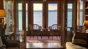 Een gezellige kamer met uitzicht op het water, met rieten stoelen, een klein tafeltje en een plafondventilator.