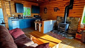 Ein gemütliches Blockhaus-Interieur mit Holzausstattung, einem Steinkamin, einer Küchenzeile und einer Sitzecke mit Couch und Tisch.