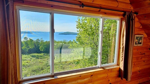 Eine Hütte mit einem großen Fenster, das einen Blick auf einen See und Wald freigibt.