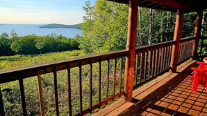 Eine Holzterrasse mit Geländer, die auf einen See und einen bewaldeten Bereich blickt.