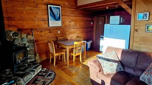 Interior acogedor de una cabaña con chimenea de piedra, mesa de comedor de madera y sofá de cuero marrón.