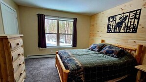 Een slaapkamer met een houten bed, een dressoir, een raam met gordijnen en een wanddecoratie.