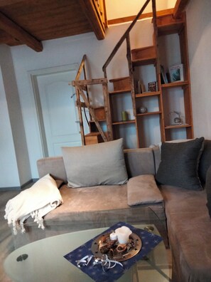 Una sala de estar con sofá, una mesa de centro de vidrio y una estantería de madera.