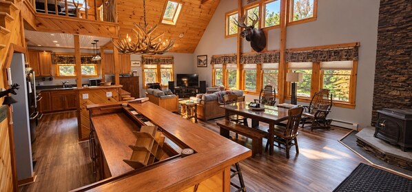 A spacious kitchen with wooden countertops and a large island, a cozy living area with a fireplace, and large windows offering views of the outdoors.