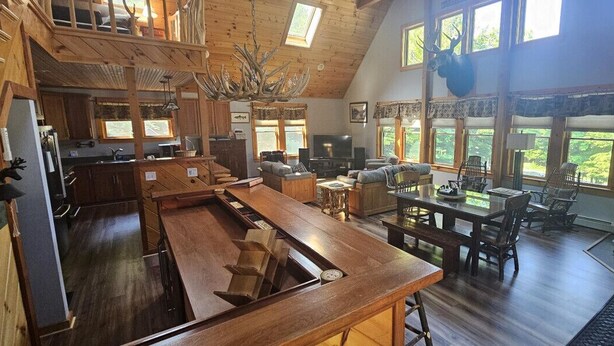 A spacious kitchen with a long island, a dining area with wooden furniture, and a stone fireplace. - Woods All Around-Direct ATV*Hot Tub*Beach Access*A/C*Pool Table*Washer/Dryer (Beaver Cove)