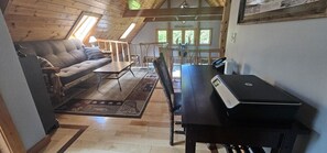 Un dormitorio acogedor en el ático con sofá, escritorio y ordenador portátil, y vistas al exterior a través de una ventana.